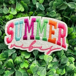 Può includere: Una toppa di feltro bianco con le parole "SUMMER vibes" ricamate in lettere colorate. La parola "SUMMER" è in rosa, turchese, magenta, verde, arancione e rosa. La parola "vibes" è in corsivo rosa.