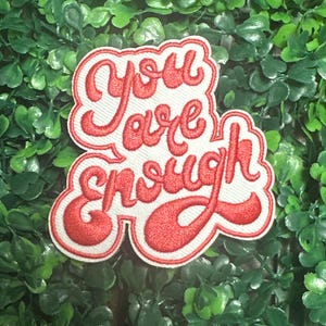 May include: White embroidered patch with red lettering that reads "You are enough".