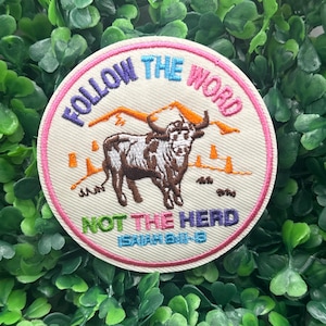 May include: Embroidered patch with a cream background, featuring a brown and white bull, orange mountains, and the text "FOLLOW THE WORD NOT THE HERD" in various colors. The patch has a pink border and the Bible verse Isaiah 6:8-13.