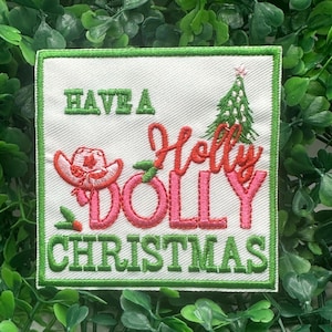May include: Embroidered patch with the text "Have a Holly Dolly Christmas." The design features a pink cowboy hat, a Christmas tree, and the words in green and pink. The patch has a white background with a green border.