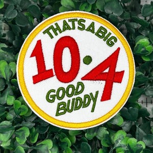 Könnte beinhalten: Runder, gestickter Aufnäher mit dem Text "THAT'S A BIG 10-4 GOOD BUDDY" in Grün und Rot auf weißem Grund, umrandet von Gelb. Der Aufnäher ist vor einem Hintergrund aus grünem Laub platziert.
