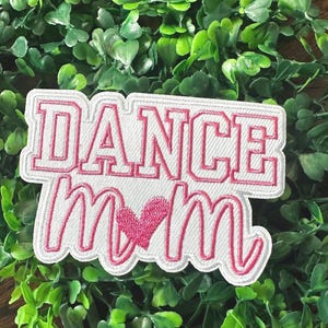 May include: White embroidered patch with pink lettering that says "Dance Mom" with a pink heart in the middle.