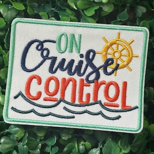Puede incluir: Parche bordado con las palabras "ON Cruise CONTROL" en verde, azul marino y naranja. Un timón amarillo está a la derecha. El parche tiene un borde verde y un diseño de olas.