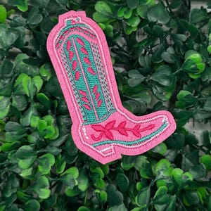 May include: Pink cowboy boot embroidered with green floral designs. The boot is a patch or iron-on.