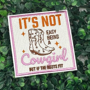 May include: Pink and white embroidered patch with brown cowboy boots and the text "It's not easy being a cowgirl, but if the boots fit".