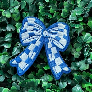 May include: A blue and white checkered bow with a white outline. The bow is made of fabric and has a stitched design.
