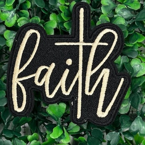 May include: Black fabric patch with the word "faith" embroidered in white thread. The word is stylized with a cross in the center of the "i".