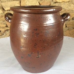 May include: A large, brown earthenware crock with two handles. The crock has a speckled glaze and is slightly weathered.
