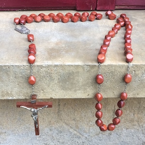 May include: A brown wooden rosary with a silver crucifix and a silver charm. The rosary is made of wooden beads and is strung on a silver chain.