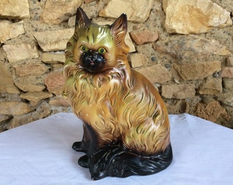 May include: A ceramic figurine of a brown and black cat with green eyes. The cat is sitting with its tail curled around its legs.