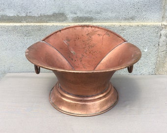 May include: A vintage copper planter with a wide, flared opening and two handles. The planter has a smooth, aged finish and a slightly rounded base.