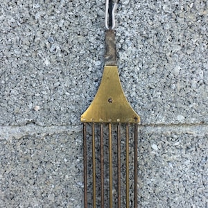 May include: A brass clock pendulum with a decorative top and a series of metal rods hanging from it.