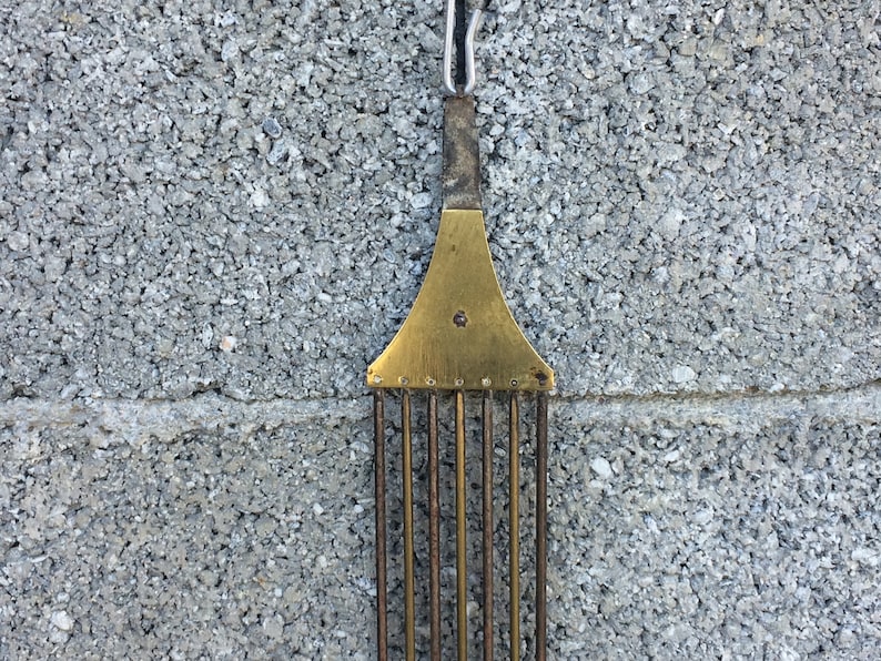 May include: A brass clock pendulum with a decorative top and a series of metal rods hanging from it.