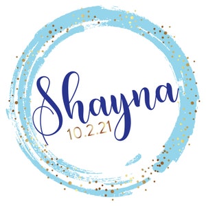 May include: A blue and gold circle with the name Shayna and the date 10.2.21 written in cursive.