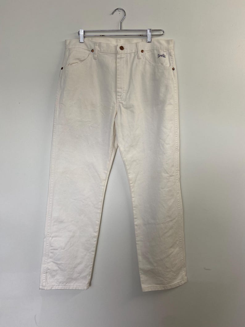 Op de afbeelding: Een paar witte rechte jeans met een klein bruin label met de tekst "Shro" op de rechter achterzak.