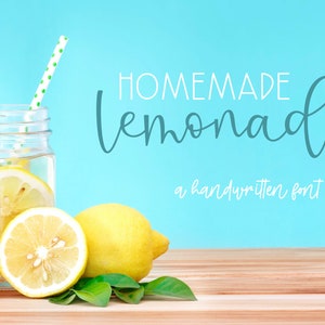 May include: A mason jar filled with lemonade and lemon slices, with a green straw sticking out of the top.  There are lemons and green leaves on a wooden surface in front of the jar. The text "HOMEMADE lemonade" is written in a handwritten font on a blue background. The text "a handwritten font duo" is written below the lemonade text.