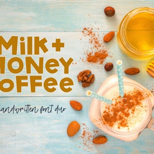 以下が含まれることがあります： 蜂蜜で満たされたガラス瓶、クリーミーな飲み物が入ったガラス瓶、木製のハチミツディッパーのクローズアップ。背景は薄い青色の木製の表面で、シナモンとナッツが散らばっています。テキスト「Milk + Honey Coffee」は手書きのフォントスタイルで書かれています。