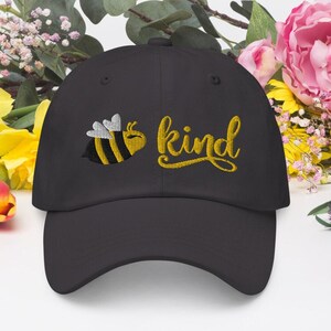 Op de afbeelding: Een zwarte baseballpet met een gele geborduurde bij en het woord "kind" in gele schrift.