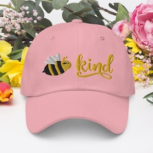 Op de afbeelding: Roze baseballpet met een geborduurde gele bij en het woord "kind" in gouden borduurwerk.
