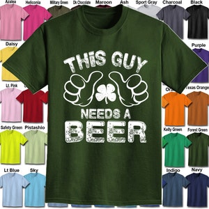 May include: A green t-shirt with a white distressed graphic that says "This Guy Needs A Beer" with a four-leaf clover in the middle of two thumbs up.