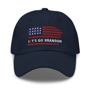 May include: Navy blue baseball cap with an embroidered American flag design. The flag features red and white stripes, with white stars on a blue background. The text "LET'S GO BRANDON" is embroidered below the flag.