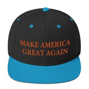 Op de afbeelding: Een zwarte en blauwe baseballpet met de tekst "MAKE AMERICA GREAT AGAIN" geborduurd in oranje.
