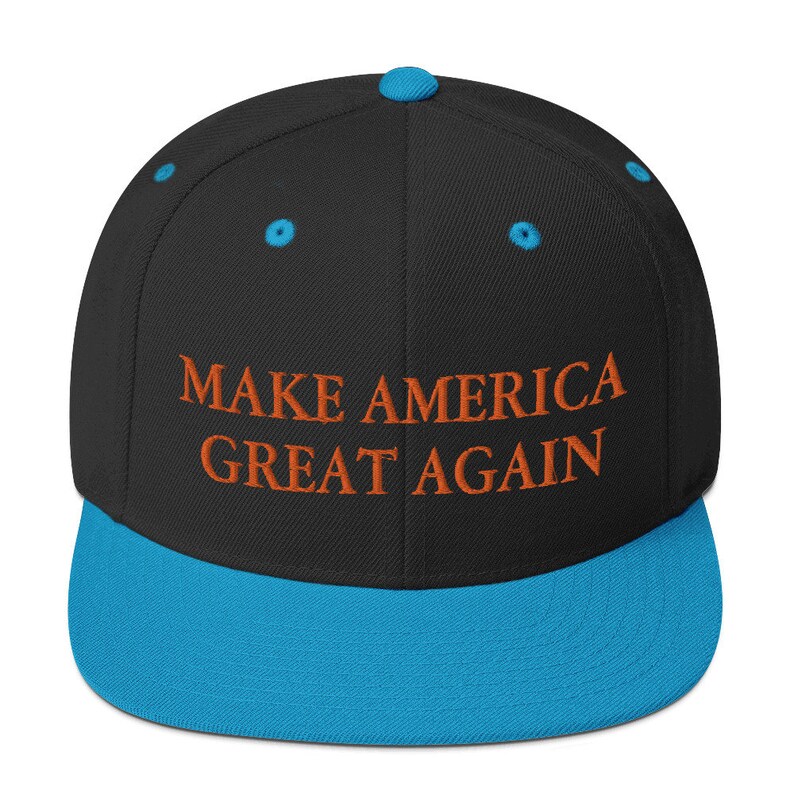 Op de afbeelding: Een zwarte en blauwe baseballpet met de tekst "MAKE AMERICA GREAT AGAIN" geborduurd in oranje.