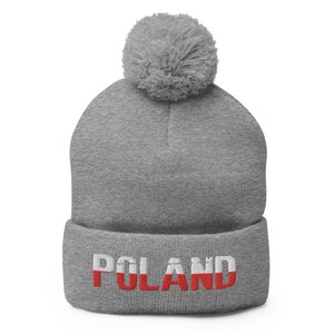 Puede incluir: Gorro gris con un pompón blanco y la palabra "POLAND" bordada en rojo y blanco, que se asemeja a la bandera polaca.