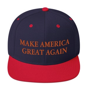 Op de afbeelding: Een marineblauwe en rode baseballpet met de tekst "MAKE AMERICA GREAT AGAIN" geborduurd in oranje.