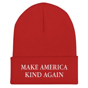 Puede incluir: Gorro de punto rojo con texto blanco que dice "Make America Kind Again".
