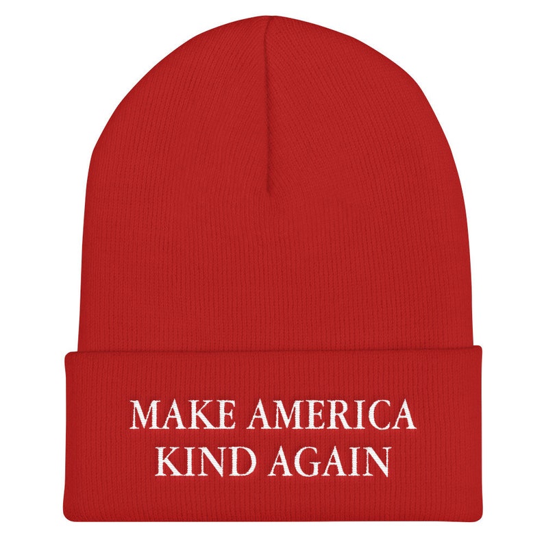 Puede incluir: Gorro de punto rojo con texto blanco que dice "Make America Kind Again".