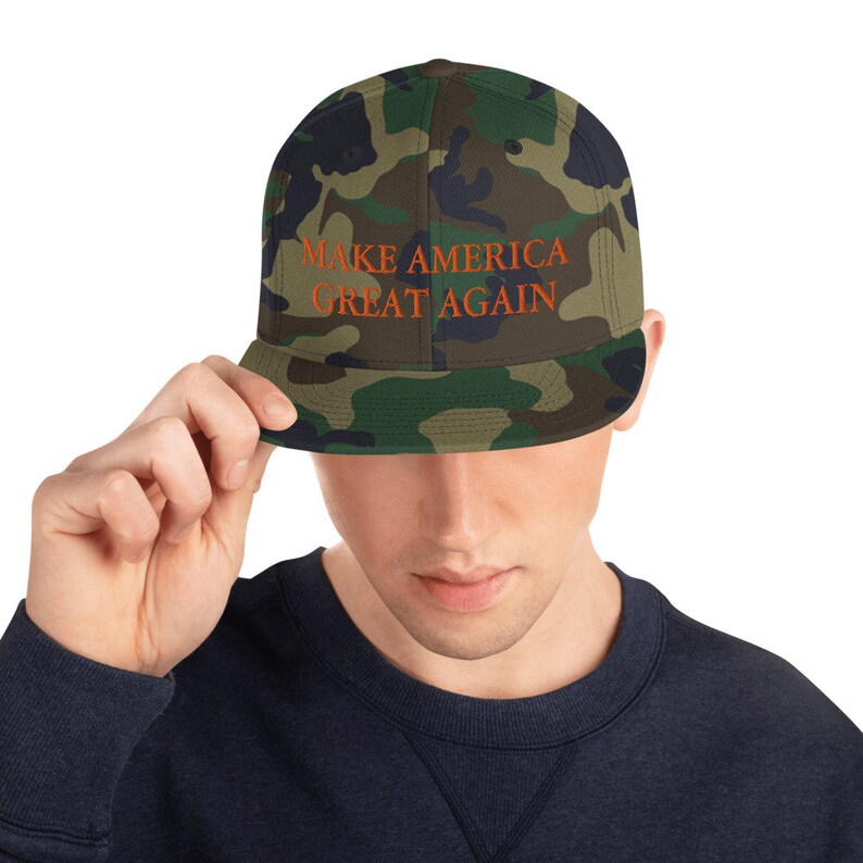Op de afbeelding: Een baseballpet met camouflagepatroon met de tekst "MAKE AMERICA GREAT AGAIN" geborduurd in oranje.