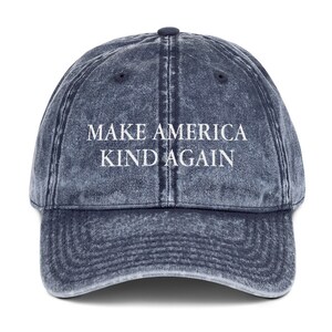 May include: A blue denim baseball cap with the text "Make America Kind Again" in white lettering.