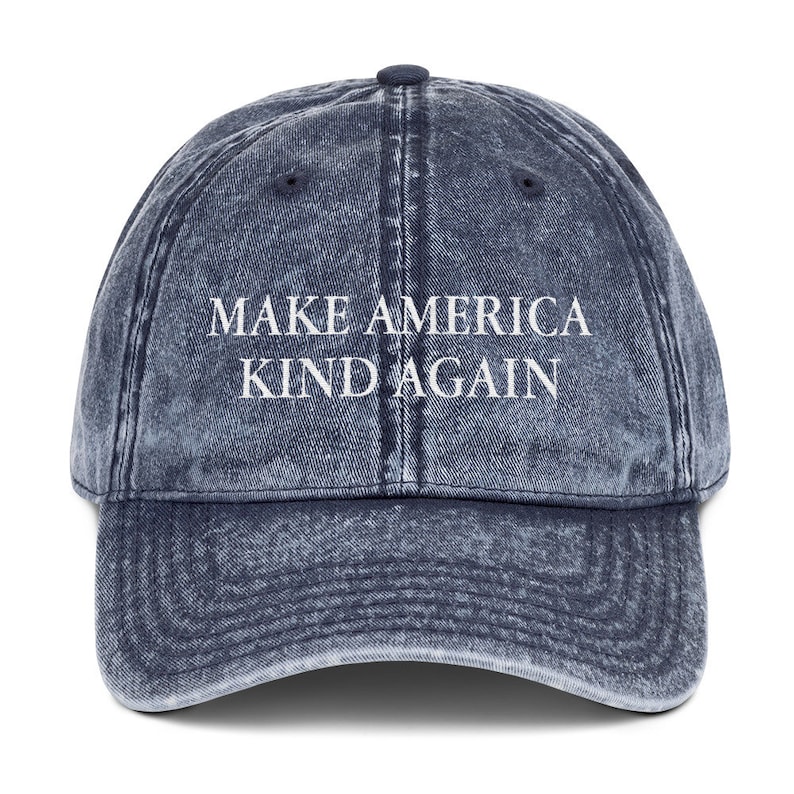 May include: A blue denim baseball cap with the text "Make America Kind Again" in white lettering.
