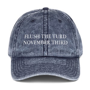 May include: A blue denim baseball cap with the text "FLUSH THE TURD NOVEMBER THIRD" embroidered in white.