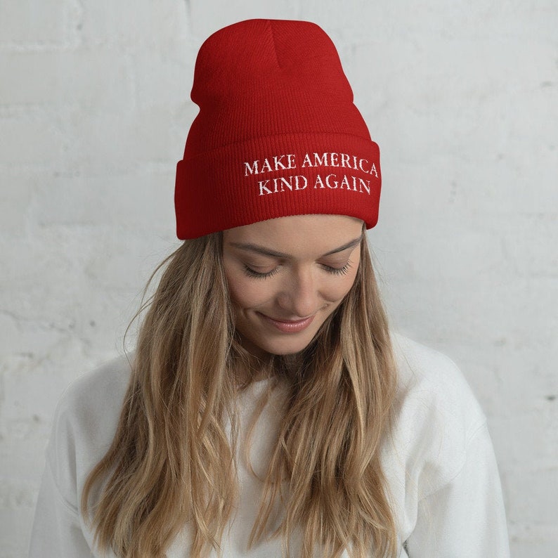 Puede incluir: Gorro de punto rojo con el texto "Make America Kind Again" en blanco.