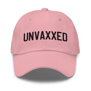 May include: A light pink baseball cap with the word "UNVAXXED" embroidered in black across the front. The cap has a curved brim and a fabric strap closure at the back.