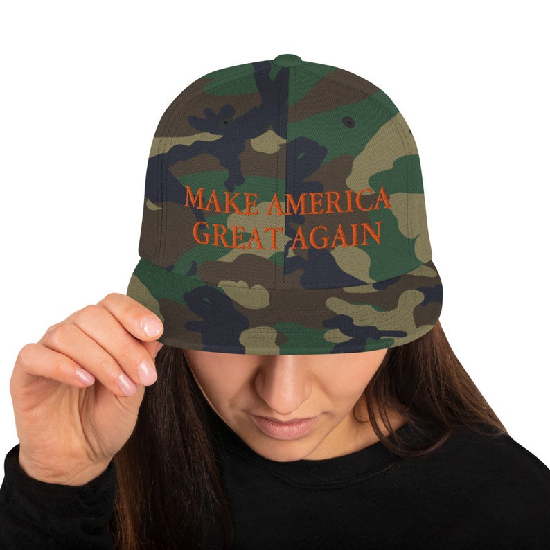 Op de afbeelding: Een camouflage baseballpet met de tekst "MAKE AMERICA GREAT AGAIN" geborduurd in oranje.