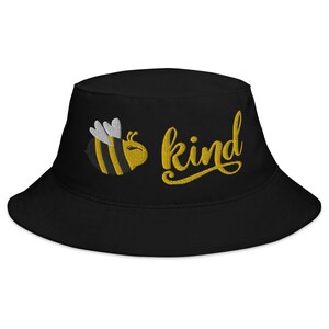 Op de afbeelding: Zwarte bucket hat met een geborduurde gele bij en het woord "be kind" in gele schrift.