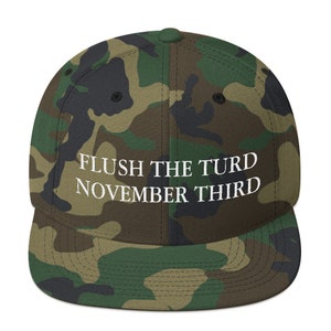 May include: A camouflage-patterned baseball cap with the text "FLUSH THE TURD NOVEMBER THIRD" embroidered in white on the front.