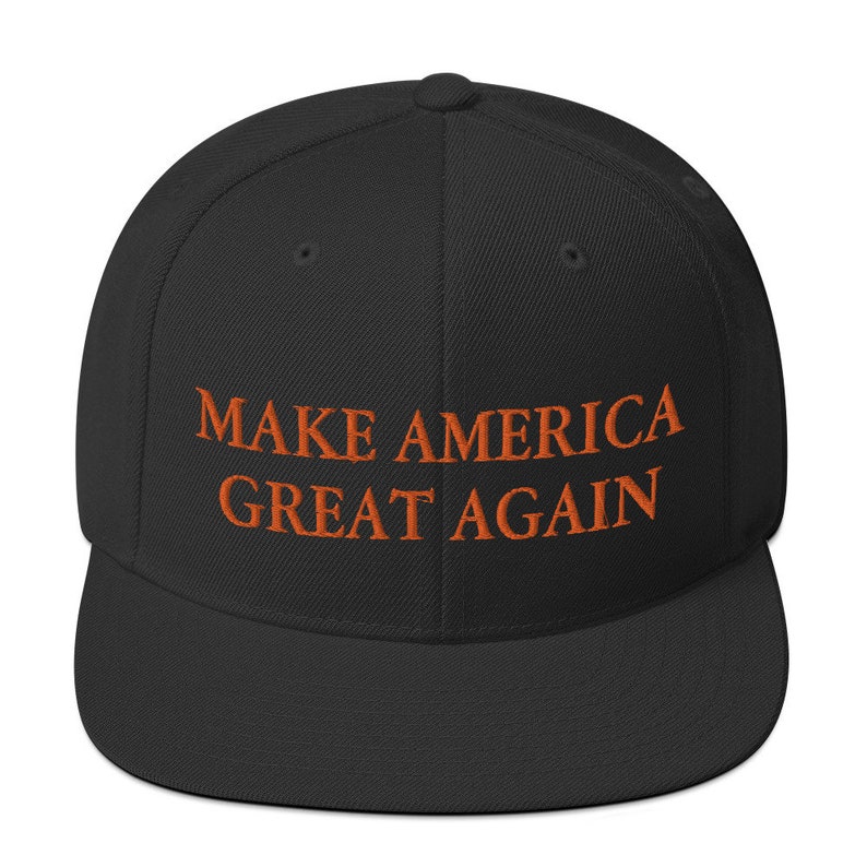 Op de afbeelding: Een zwarte baseballpet met de tekst "MAKE AMERICA GREAT AGAIN" geborduurd in oranje.