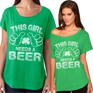 以下が含まれることがあります： 「This Girl Needs a Beer」とクローバーが書かれた白いグラフィックプリントが施された緑色のTシャツ2枚。ゆったりとしたフィット感とオフショルダーのスタイルです。