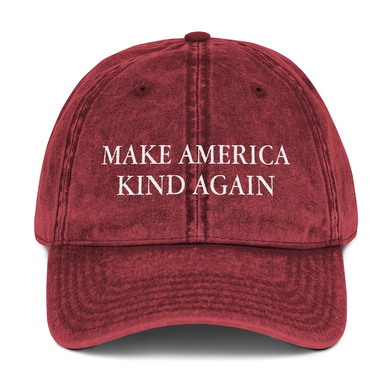 May include: A red vintage baseball cap with the text "Make America Kind Again" embroidered in white.