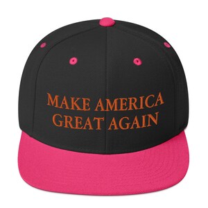 Op de afbeelding: Zwarte en roze baseballpet met de tekst "MAKE AMERICA GREAT AGAIN" geborduurd in oranje.