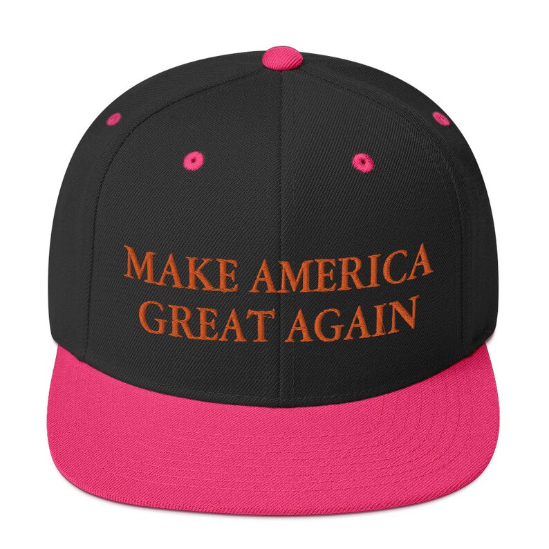 Op de afbeelding: Zwarte en roze baseballpet met de tekst "MAKE AMERICA GREAT AGAIN" geborduurd in oranje.