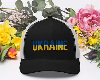 May include: A black and white trucker hat with a yellow and blue embroidered Ukrainian flag and the word "UKRAINE" in yellow.
