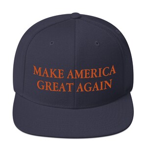 Op de afbeelding: Een marineblauwe baseballpet met de tekst "MAKE AMERICA GREAT AGAIN" geborduurd in oranje.