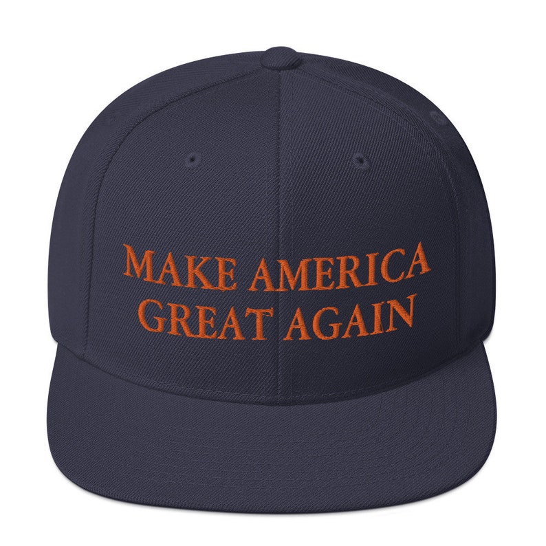 Op de afbeelding: Een marineblauwe baseballpet met de tekst "MAKE AMERICA GREAT AGAIN" geborduurd in oranje.