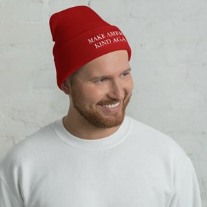 Puede incluir: Un gorro de punto rojo con el texto "MAKE AMERICA KIND AGAIN" en letras blancas.