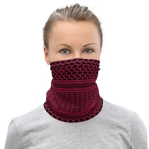 May include: A maroon and black face covering with a geometric pattern. The neck gaiter is worn around the neck and covers the lower face. The fabric has a repeating design of black shapes on a maroon background. The person is wearing a gray shirt.